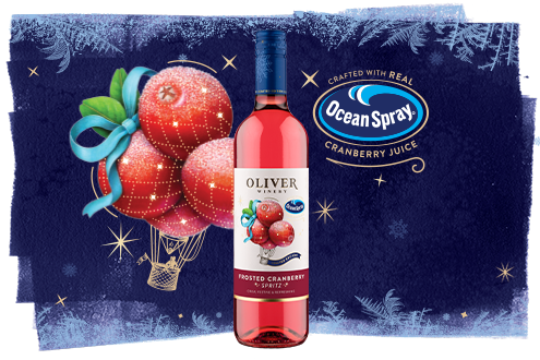 A bottle of Oliver Winery Frosted Cranberry Spritz on a deep blue frosted background, beside an illustration of sugared cranberries carried by a hot air balloon and a seal reading Crafted with Real Ocean Spray Cranberry Juice.