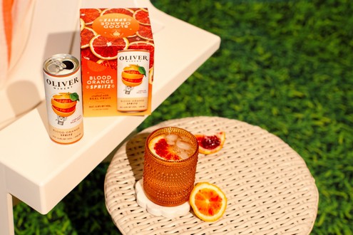 Oliver Winery Blood Orange Spritz can, 4-pack and a glass of spritz over ice on a sunny patio