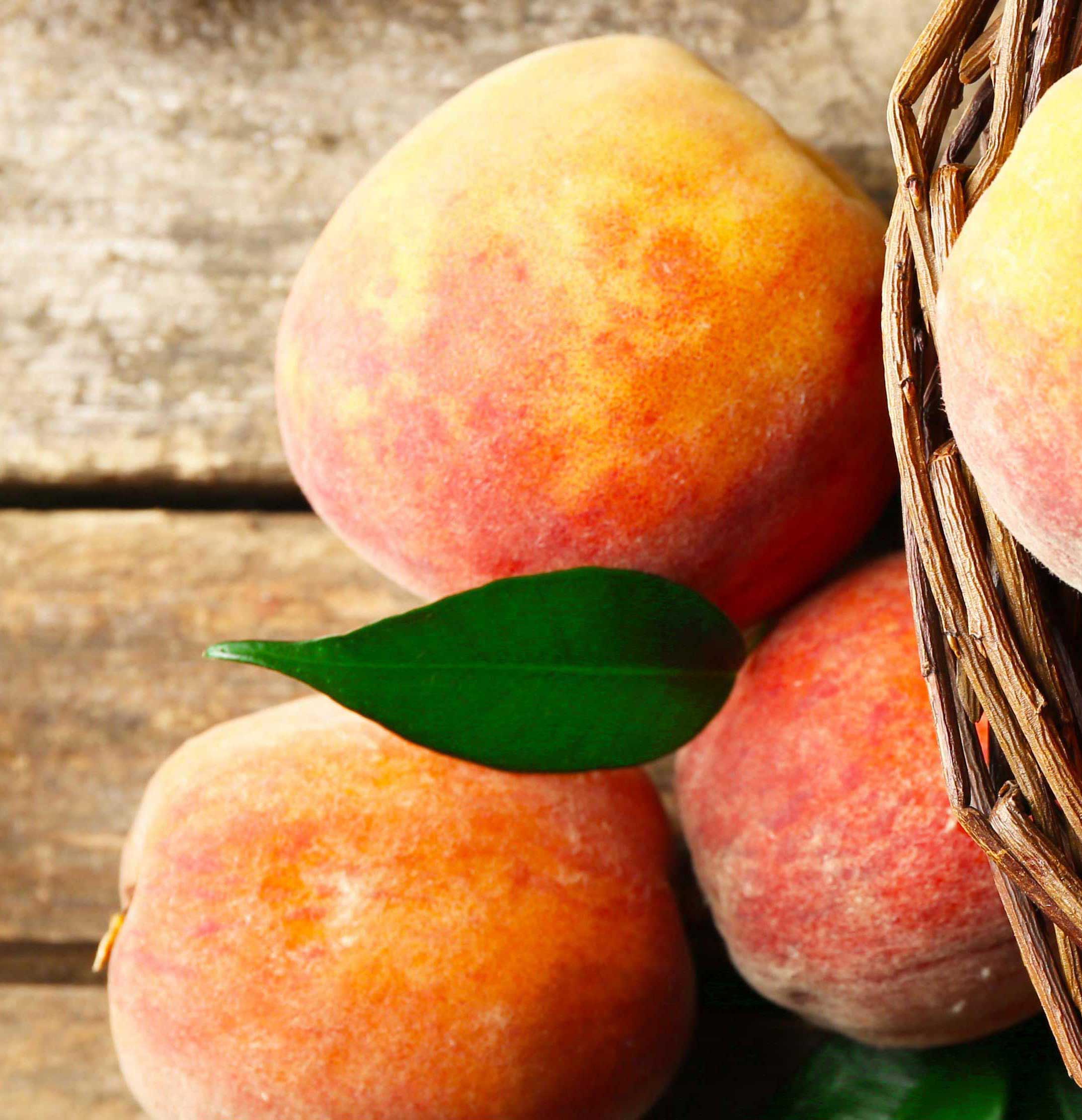 Ripe, fresh peaches in a basket, representing the flavor of new Peach Pie wine from Oliver Winery.