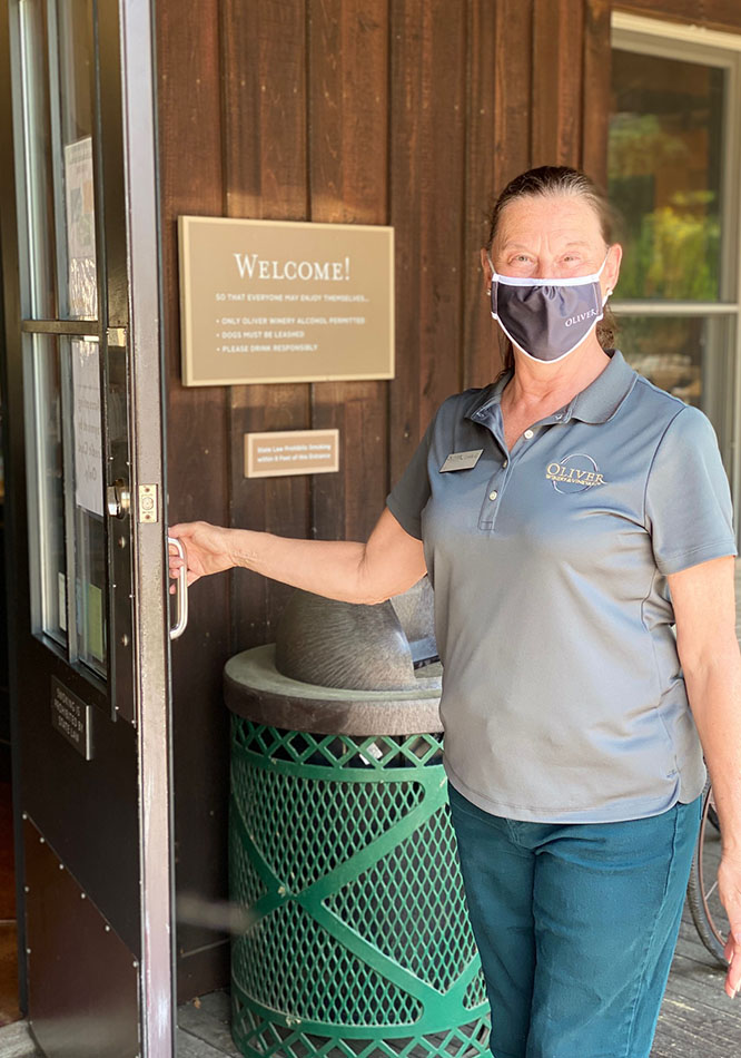 A masked tasting room staffer holds the door for incoming guests.