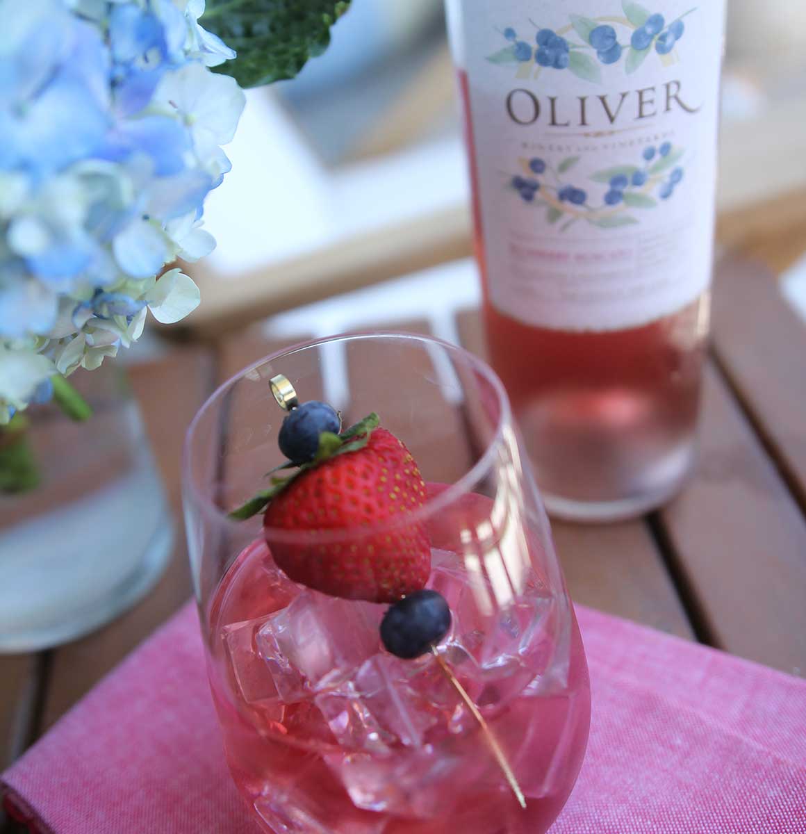 Oliver Blueberry Moscato in a stemless wine glass with red, white, and blue fruit garnish.