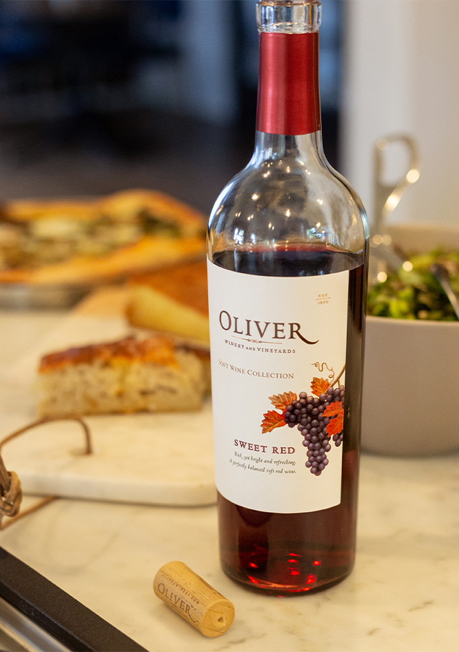 A bottle of Oliver Sweet Red on a counter with bread and a salad.