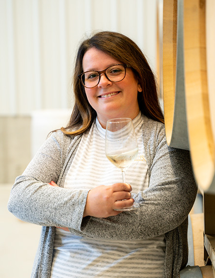 Lora Pennington poses in front of Oliver Winery barrels with one of her favorite wines, Creekbend Vignoles.