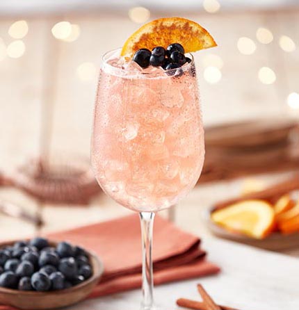 Oliver Blueberry Moscato cocktail the Cinnaberry Spritz prepared in a wine glass over ice, garnished with an orange slice.