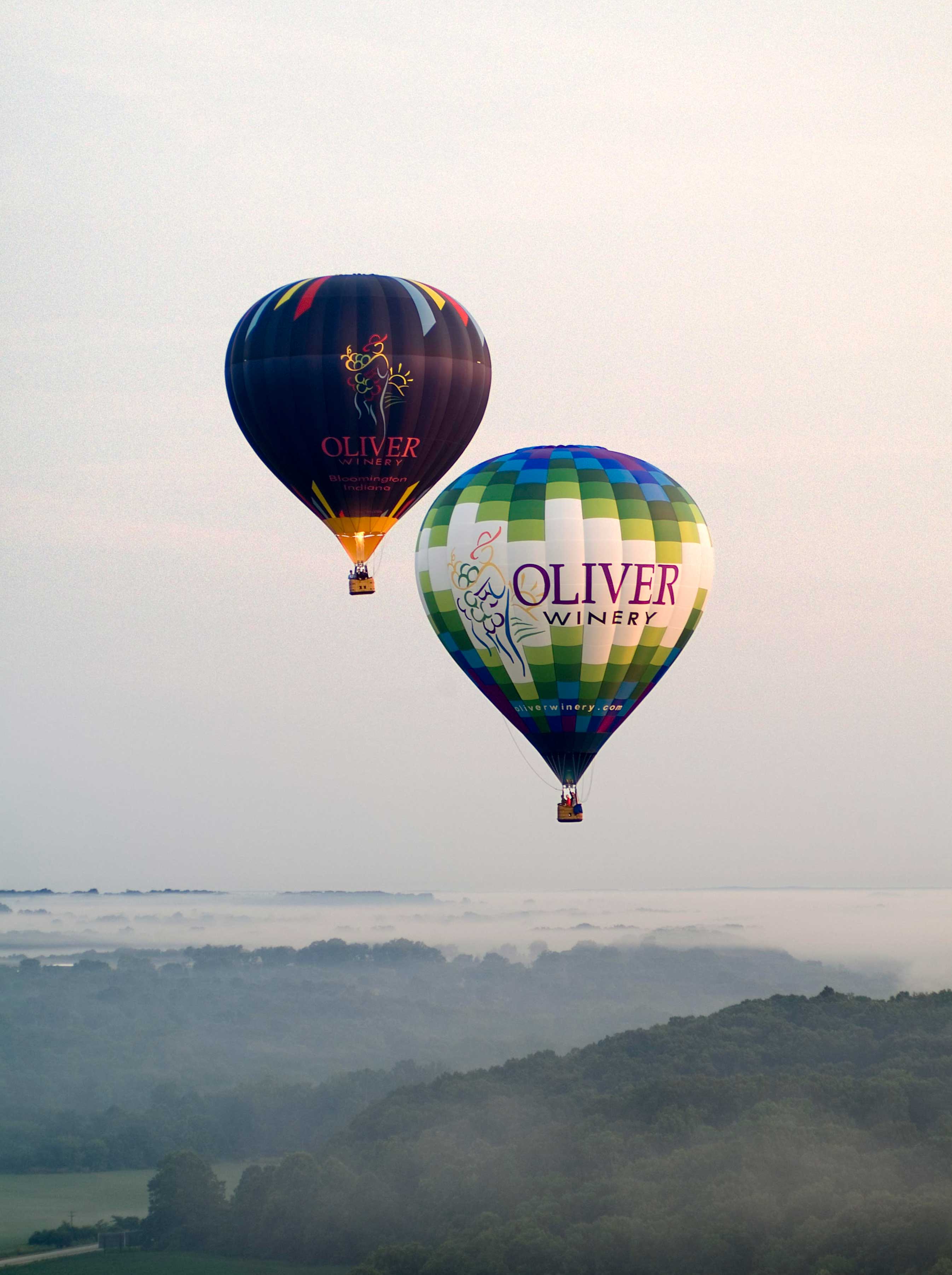 A pair of Oliver Winery hot air balloons float in the sky. 
