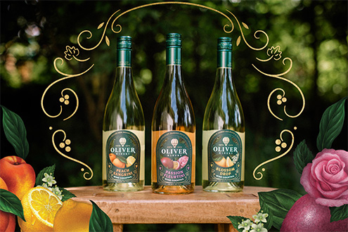 Introducing Oliver Winery's newest line of ready-to-drink Signature Cocktails. Three cocktail bottles sit in a lush garden setting, surrounded by swirling gold filigree and fruit illustrations.