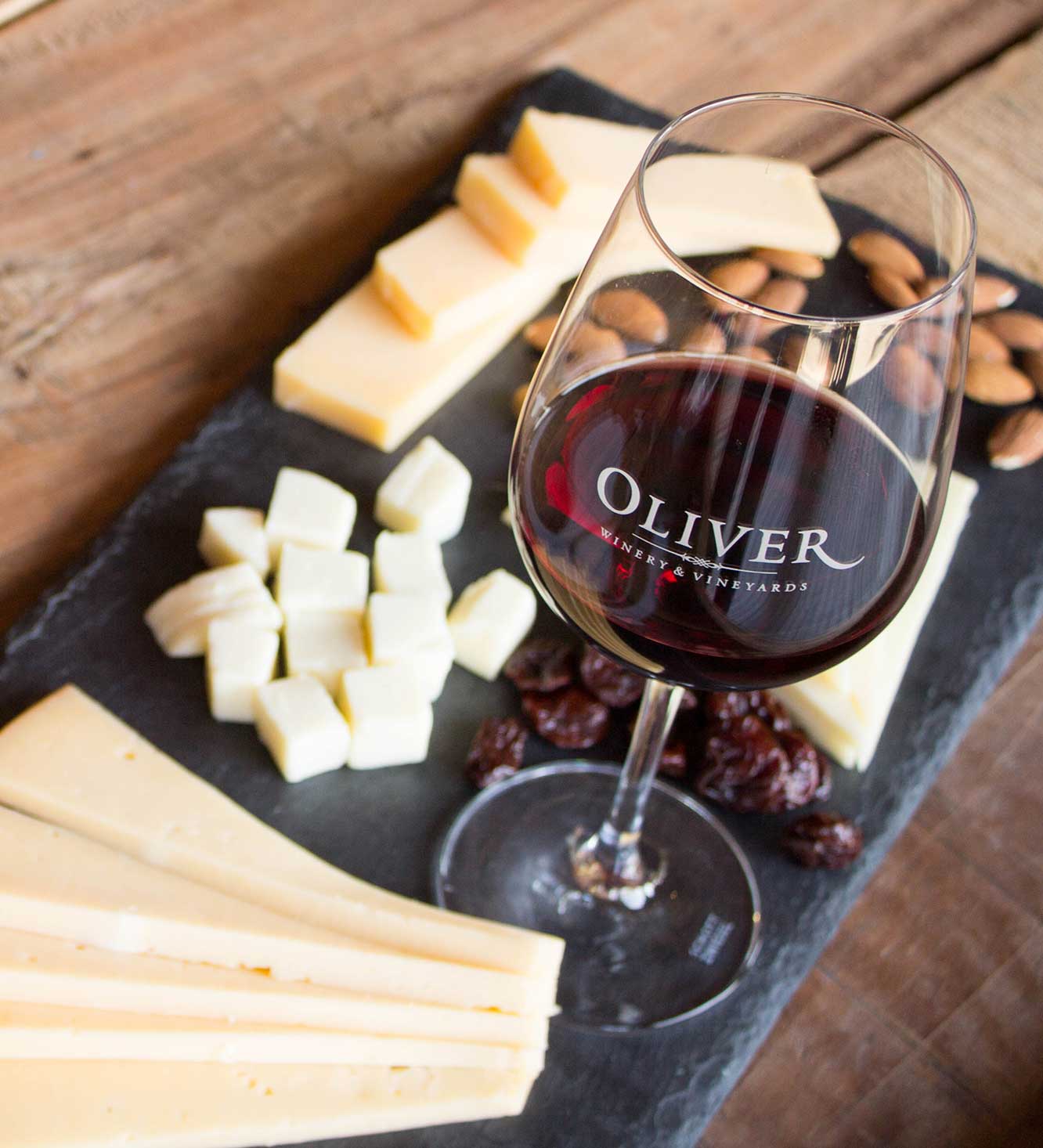 Oliver Dry Red Blend, a blend of Cabernet Sauvignon and Syrah, poured in a glass next to a slate cheese board.