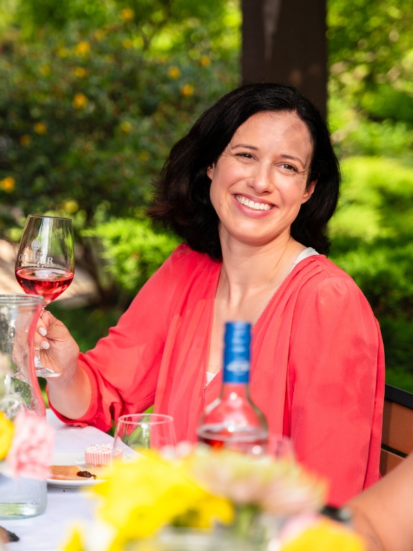 A smiling guest raises a glass of rosé at an outdoor table at Oliver Winery.
