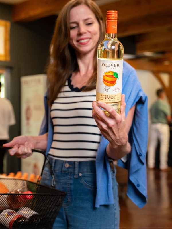 A smiling shopper holds up a bottle of Oliver Blood Orange Spritz in the tasting room.