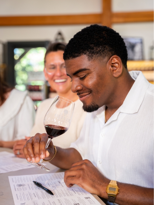 A guest smiles as he tilts a glass of red wine at the Oliver Winery tasting bar.