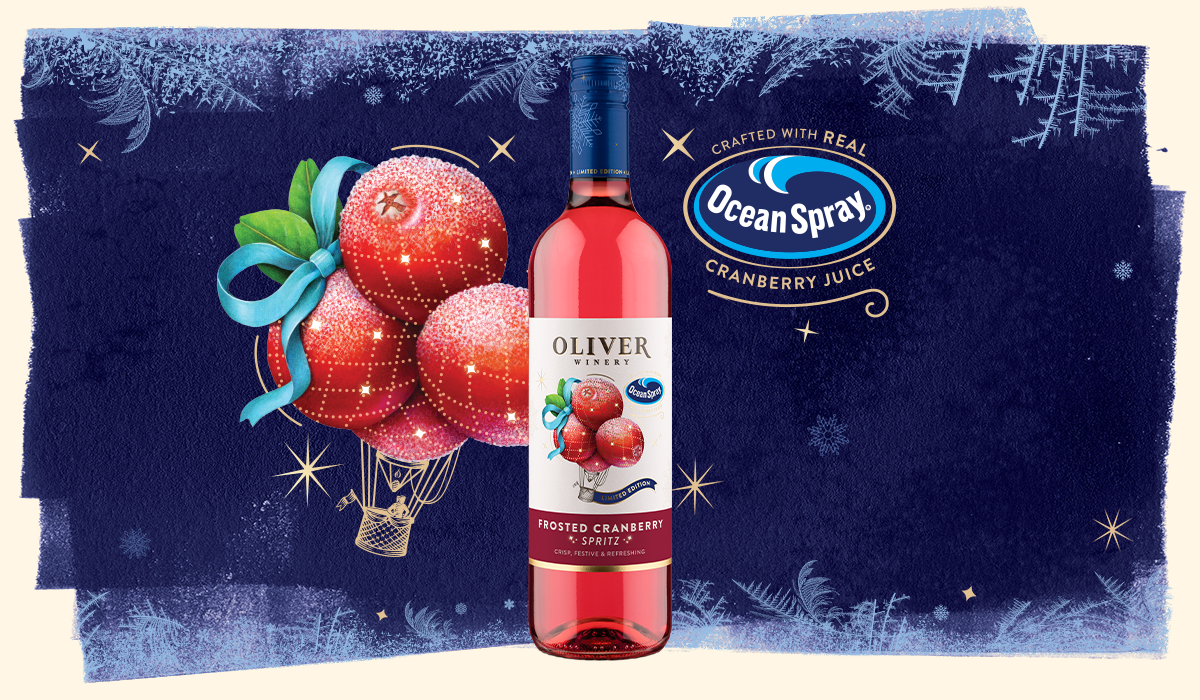 A bottle of Oliver Winery Frosted Cranberry Spritz on a deep blue frosted background, beside an illustration of sugared cranberries carried by a hot air balloon and a seal reading Crafted with Real Ocean Spray Cranberry Juice.